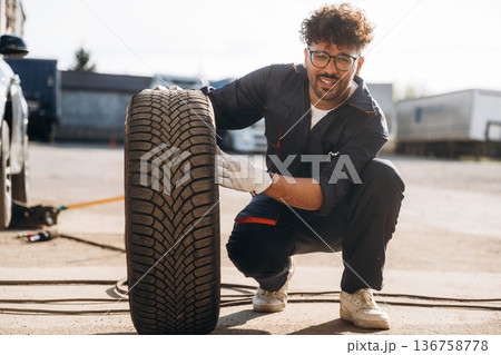 Looking forward, with tire. Mechanic is with the car outdoors Looking forward, with tire. Mechanic is with the car outdoors 136758778