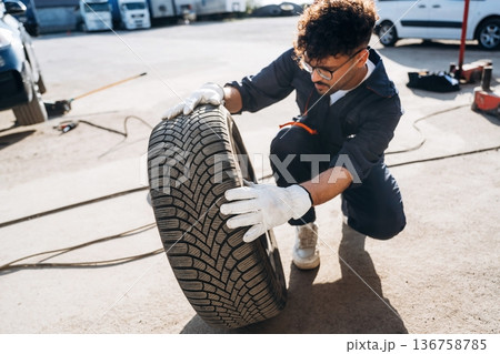 Checking the tire. Mechanic is with the car outdoors 136758785