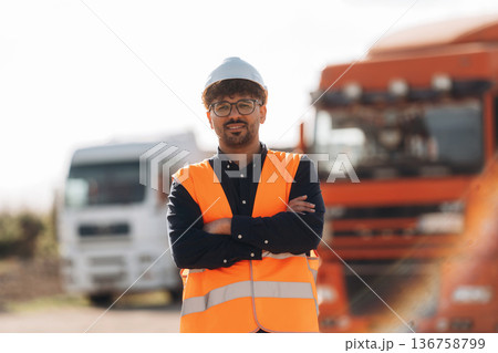 Standing with arms crossed. Male worker is near truck outdoors Standing with arms crossed. Male worker is near truck outdoors 136758799