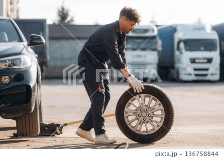 Outdoors with new tire. Mechanic is with the car Outdoors with new tire. Mechanic is with the car 136758844