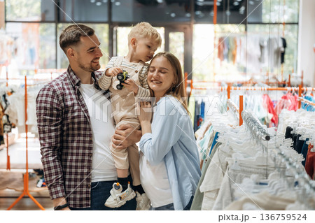 Conception of love and care. Father, son and pregnant mother are in kid's clothing store Conception of love and care. Father, son and pregnant mother are in kid's clothing store 136759524