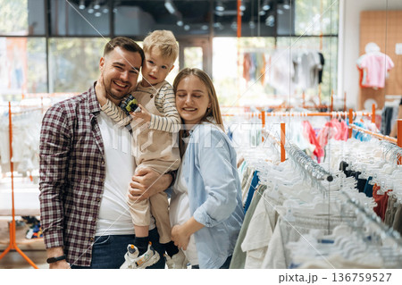 Standing and smiling. Father, son and pregnant mother are in kid's clothing store 136759527