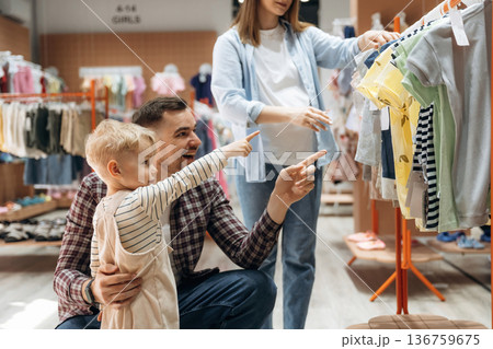 Choosing the wear. Father, son and pregnant mother are in kid's clothing store 136759675