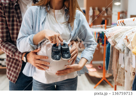 Pregnant woman with man are in the kid's clothing store Pregnant woman with man are in the kid's clothing store 136759713