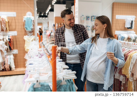 Positive facial expressions. Pregnant woman with man are in the kid's clothing store Positive facial expressions. Pregnant woman with man are in the kid's clothing store 136759714