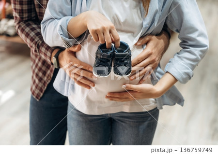 Embracing, holding little shoes. Pregnant woman with man are in the kid's clothing store Embracing, holding little shoes. Pregnant woman with man are in the kid's clothing store 136759749