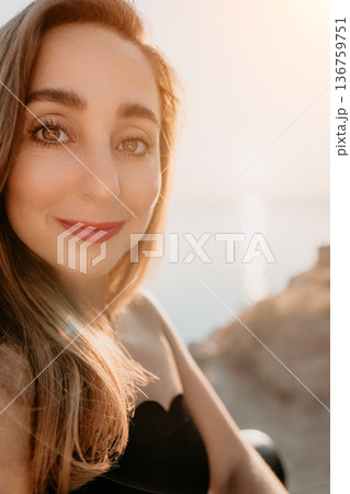 Woman portrait sunset smiling during golden hour on a coast overlooking the sea with warm natural light 136759751