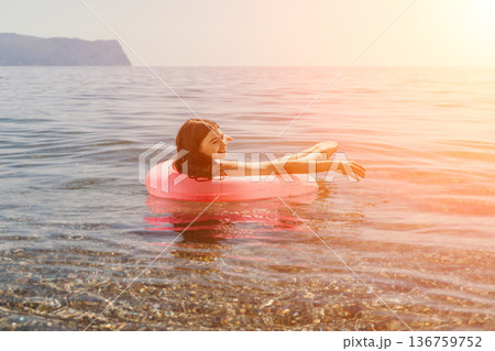 Woman floating sea happy young girl relaxing on a pink inflatable ring in the calm ocean water during sunset Woman floating sea happy young girl relaxing on a pink inflatable ring in the calm ocean water during sunset 136759752