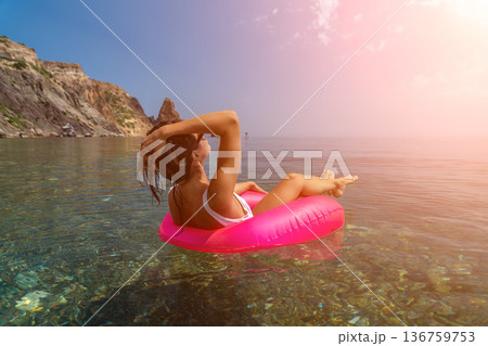 Woman floating clear water, relaxing on pink inflatable ring near stunning mediterranean cliffs enjoying tranquil summer vacation Woman floating clear water, relaxing on pink inflatable ring near stunning mediterranean cliffs enjoying tranquil summer vacation 136759753