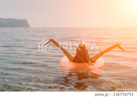 Woman ocean inflatable floating in calm sea with arms outstretched during a golden sunset reflecting vacation and freedom Woman ocean inflatable floating in calm sea with arms outstretched during a golden sunset reflecting vacation and freedom 136759755