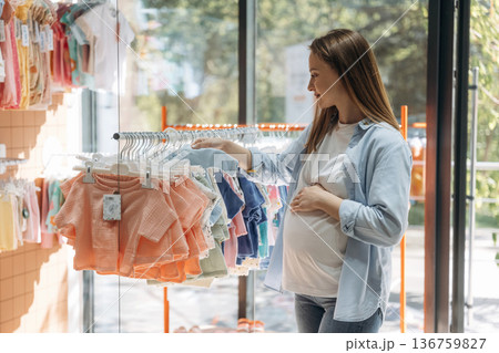 Choice of the big amount of wear. Young pregnant woman is in the kid's clothing store Choice of the big amount of wear. Young pregnant woman is in the kid's clothing store 136759827
