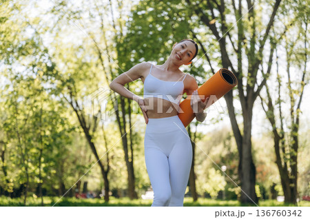 Holding yoga mat. Beautiful fitness woman is outdoors, amazing nature 136760342