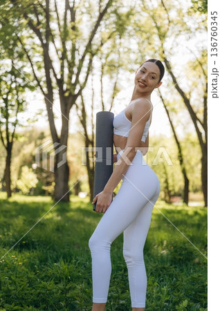 Holding yoga mat. Beautiful fitness woman is outdoors, amazing nature 136760345