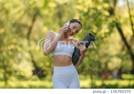 Using phone. Beautiful fitness yoga woman is outdoors, amazing nature Using phone. Beautiful fitness yoga woman is outdoors, amazing nature 136760370