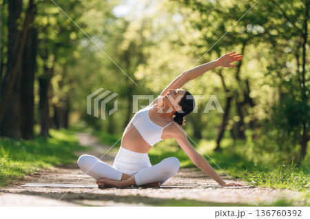 Mat is on the pathway, sitting. Beautiful fitness yoga woman is outdoors, amazing nature Mat is on the pathway, sitting. Beautiful fitness yoga woman is outdoors, amazing nature 136760392