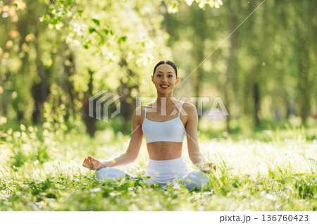 Feeling good, sitting on the grass and doing exercise. Beautiful fitness yoga woman is outdoors, amazing nature Feeling good, sitting on the grass and doing exercise. Beautiful fitness yoga woman is outdoors, amazing nature 136760423