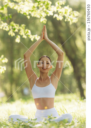 Arms raised up, sitting on the grass. Beautiful fitness yoga woman is outdoors, amazing nature Arms raised up, sitting on the grass. Beautiful fitness yoga woman is outdoors, amazing nature 136760430