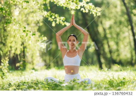 Arms raised up, sitting on the grass. Beautiful fitness yoga woman is outdoors, amazing nature 136760432