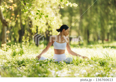 Feeling good, sitting on the grass and doing exercise. Beautiful fitness yoga woman is outdoors, amazing nature Feeling good, sitting on the grass and doing exercise. Beautiful fitness yoga woman is outdoors, amazing nature 136760613
