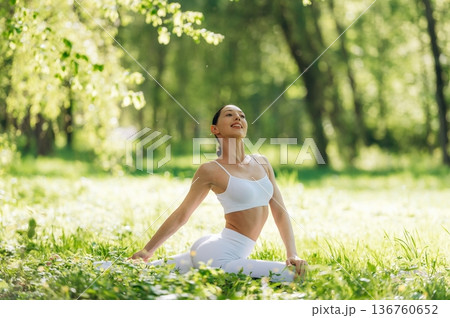 Feeling good, sitting on the grass and doing exercise. Beautiful fitness yoga woman is outdoors, amazing nature 136760652