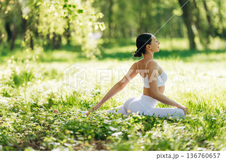 Side view, sitting on the grass. Beautiful fitness yoga woman is outdoors, amazing nature 136760657