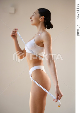 Results of diet, measuring the waist. Young woman in sportive clothes is against the wall Results of diet, measuring the waist. Young woman in sportive clothes is against the wall 136761155