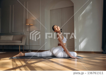 Stretching the legs. Young woman in fitness clothes is in the room 136761311