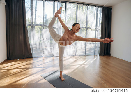 One leg is up, standing. Young woman in fitness clothes is in the room One leg is up, standing. Young woman in fitness clothes is in the room 136761413