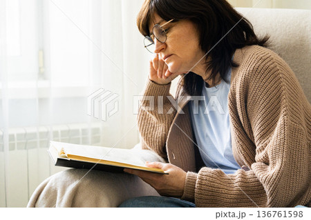 Woman wearing glasses reading book at home Woman wearing glasses reading book at home 136761598