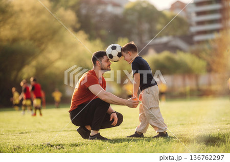 Keeping soccer ball by heads. Father and son are having fun outdoors 136762297