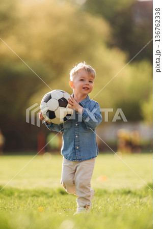 In blue shirt, with soccer ball. Little boy is having fun on the field outdoors 136762338