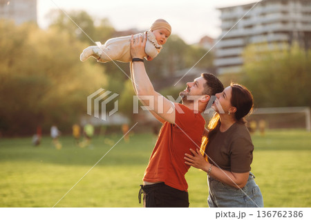 Positive facial expression. Happy couple parents are with little baby outdoors Positive facial expression. Happy couple parents are with little baby outdoors 136762386