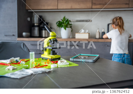 Home science experiment workspace with microscope and tools while child washing hands in background. Responsible STEM learning and laboratory safety at home. Home science experiment workspace with microscope and tools while child washing hands in background. Responsible STEM learning and laboratory safety at home. 136762452