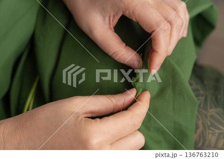 Woman darning a green jacket by hand with needle and patch fabric 136763210