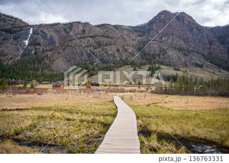 Wooden trail over marshy terrain near Blue Geyser Lake Aktash Altai Russia. Nature path guiding visitors to volcanic lake 136763331