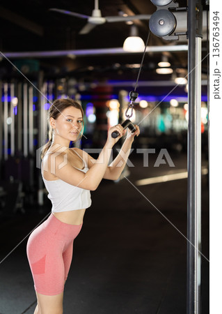 Slender athletic woman work out muscles of hands on cable crossover machine in fitness club 136763494