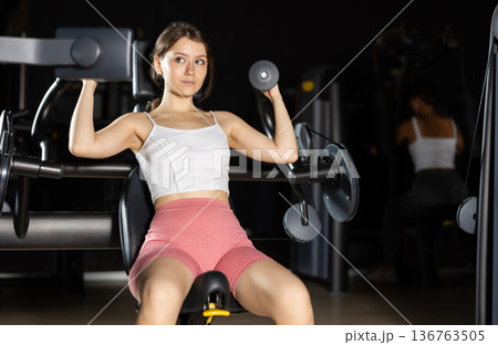 Young woman training her arms on machine Young woman training her arms on machine 136763505