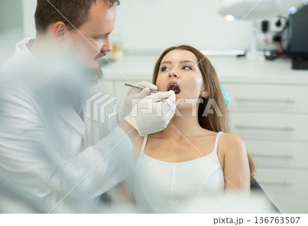 Male doctor checks young woman teeth during visit to dental clinic 136763507