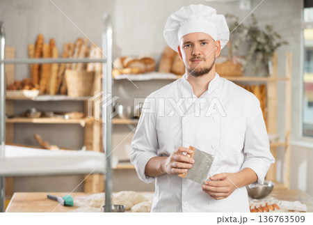 Male baker stands near work table in bakery, resting while working. Male baker stands near work table in bakery, resting while working. 136763509