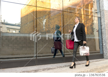 Businesswoman walking by glass wall with reflection 136763536
