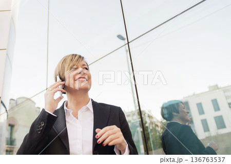 Businesswoman on phone by modern glass building 136763537