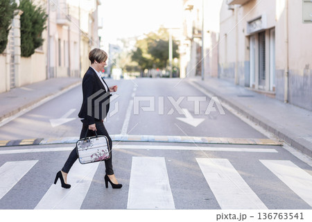 Businesswoman crossing street with briefcase Businesswoman crossing street with briefcase 136763541
