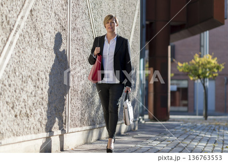 Businesswoman walking outdoors with handbags 136763553