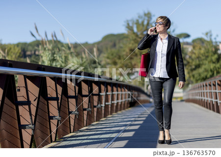 Businesswoman walking on bridge talking on phone 136763570