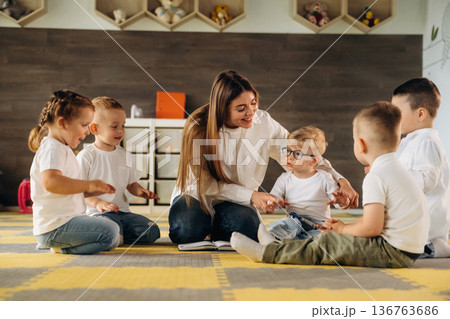 On the floor, learning new words. Children in kindergarten with their teacher 136763686