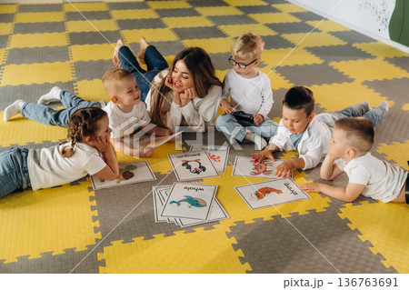 Lying down on floor, learning new words. Children in kindergarten with their teacher Lying down on floor, learning new words. Children in kindergarten with their teacher 136763691