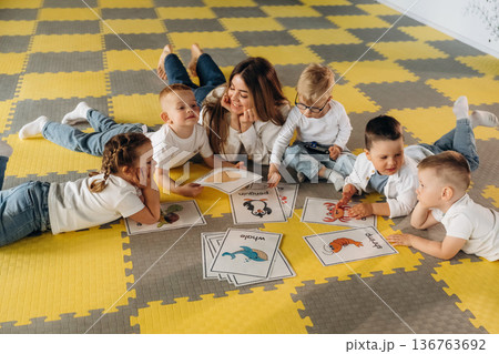 Lying down on floor, learning new words. Children in kindergarten with their teacher 136763692