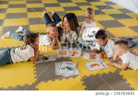 Lying down on floor, learning new words. Children in kindergarten with their teacher 136763693