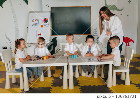 White table, sitting and learning. Children in kindergarten with their teacher 136763731
