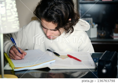 Teenage Boy Studying At Home Focused On Homework At Desk In Cozy Evening 136763798